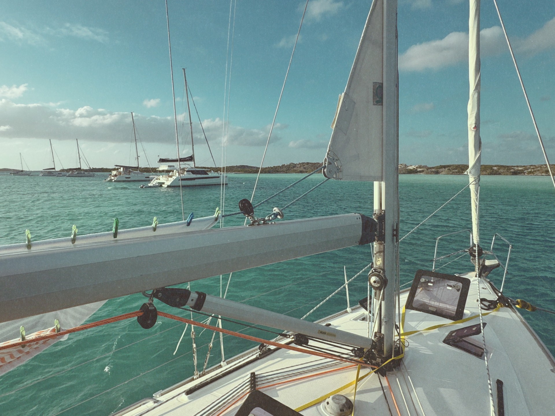Looking forward from the foredeck of a cruising sailboat into the Warderick Wells mooring field, with other boats on their moorings and low cays on the horizon.